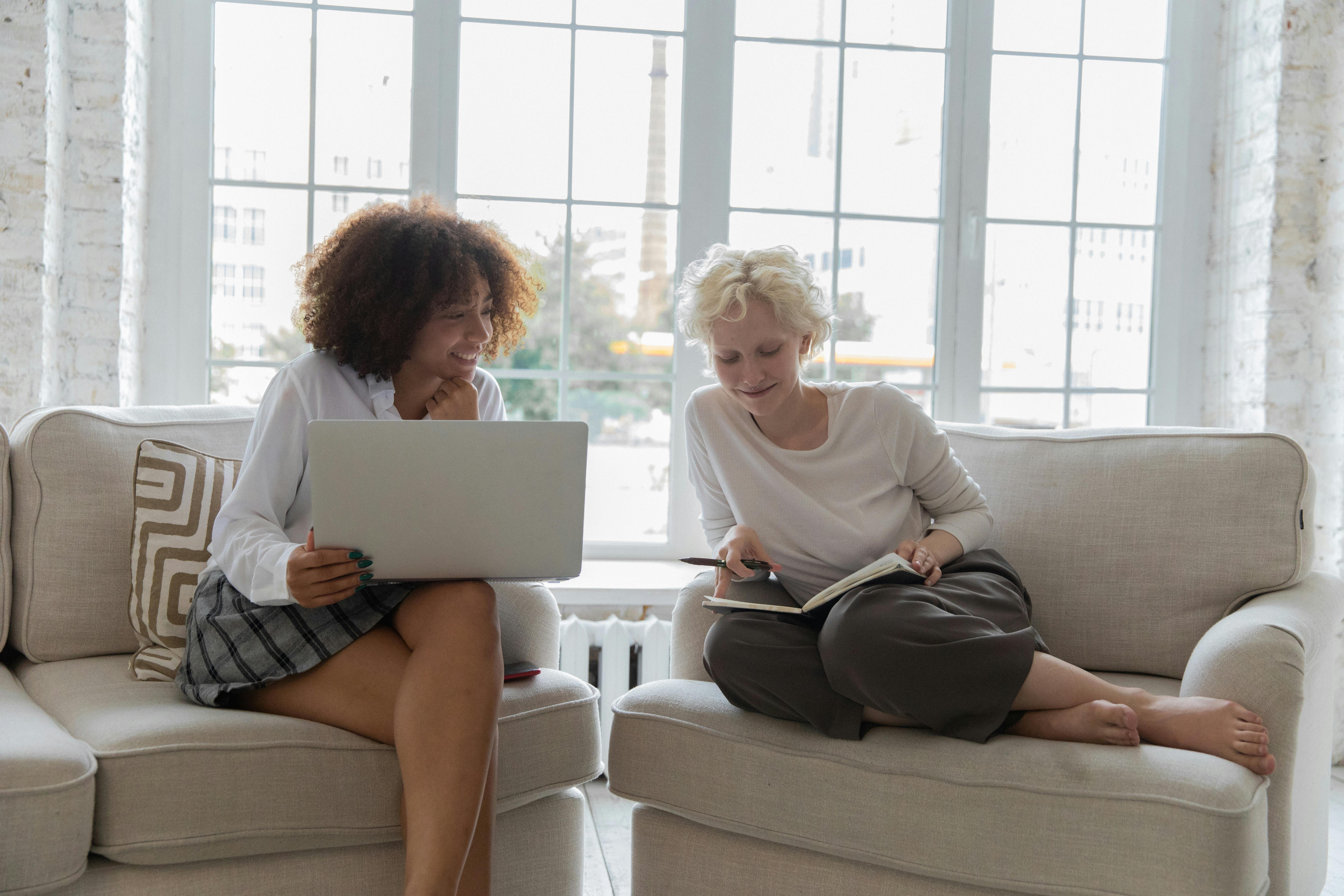 cheerful young multiethnic girlfriends discussing project while working on netbook at home