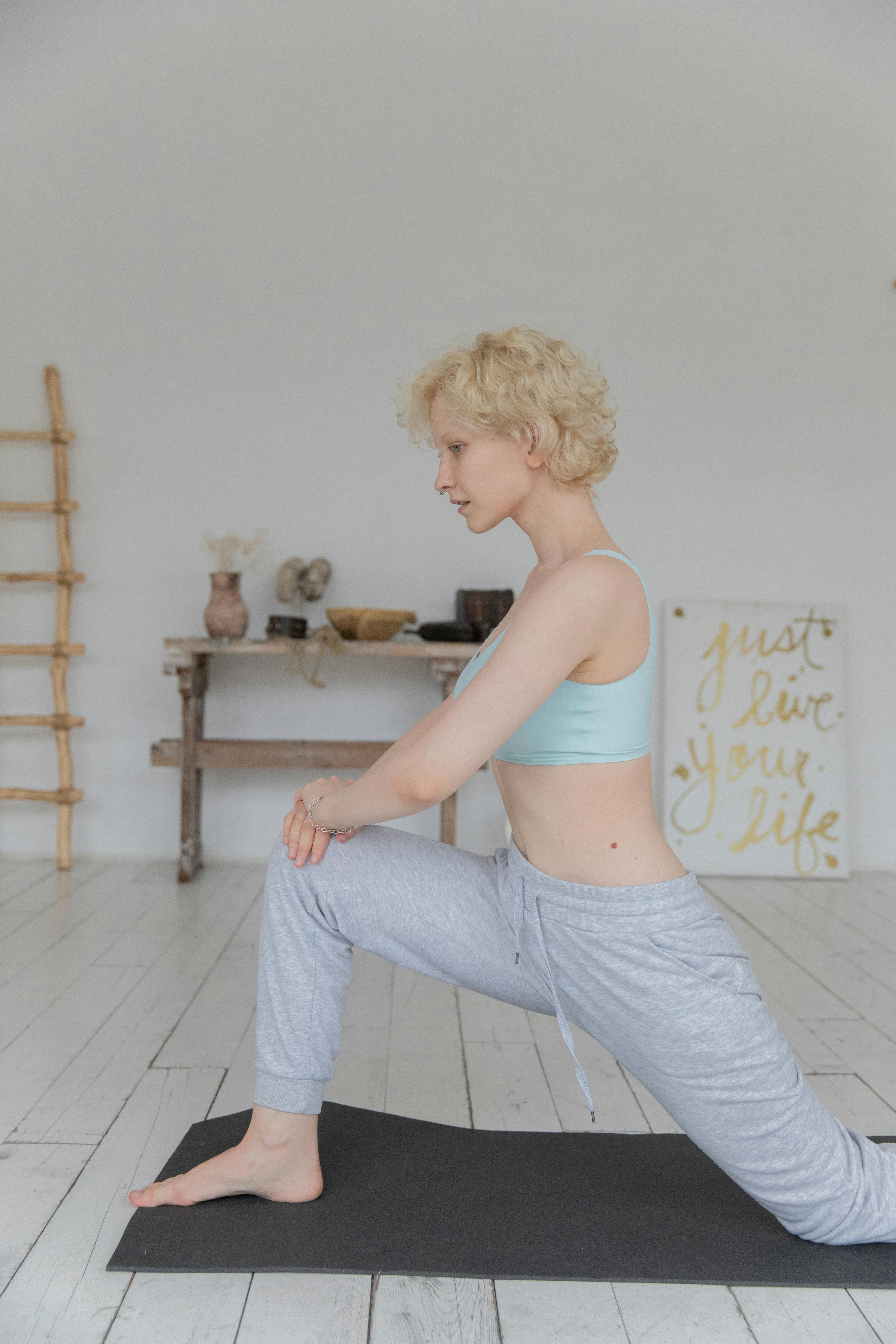 slim young woman performing anjaneyasana yoga pose on mat at home