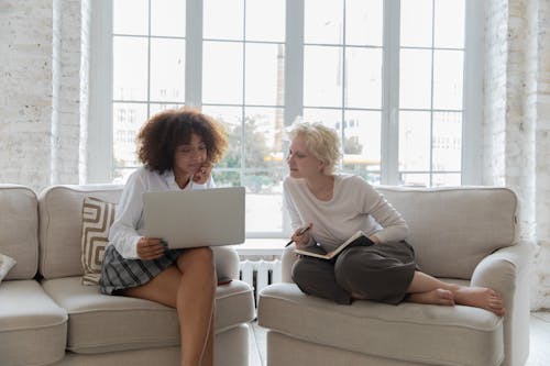 Free Positive young diverse girlfriends working on project together using laptop in apartment Stock Photo