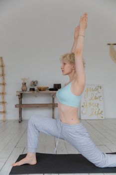Side view of young slender female in sportswear doing Crescent Lunge on the Knee asana while practicing yoga in cozy room in morning