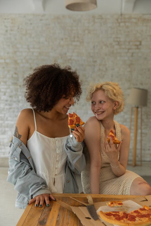 Happy young diverse girlfriends enjoying tasty pizza together at home