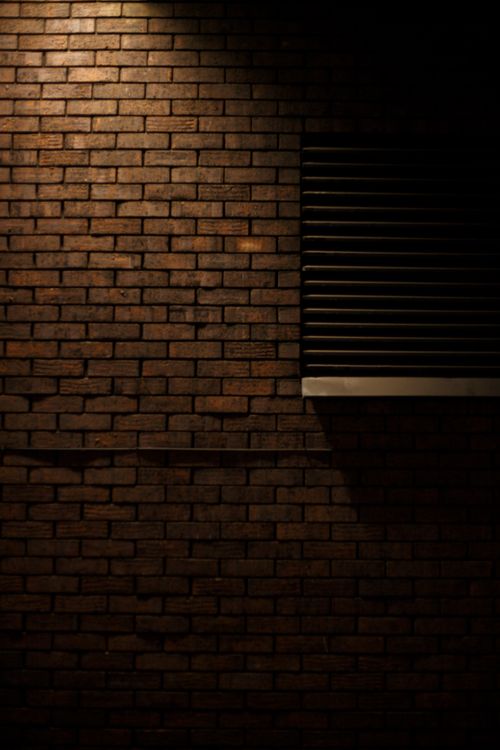 Free A dimly lit brick wall with a moody texture and shadow elements. Stock Photo