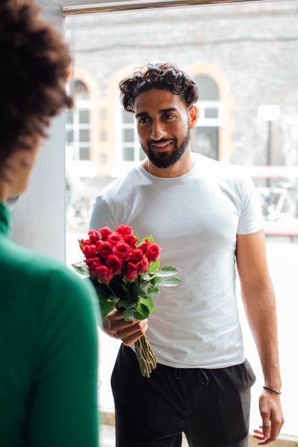 Smiling man offering a bouquet of red roses at the doorway, expressing happiness and affection.