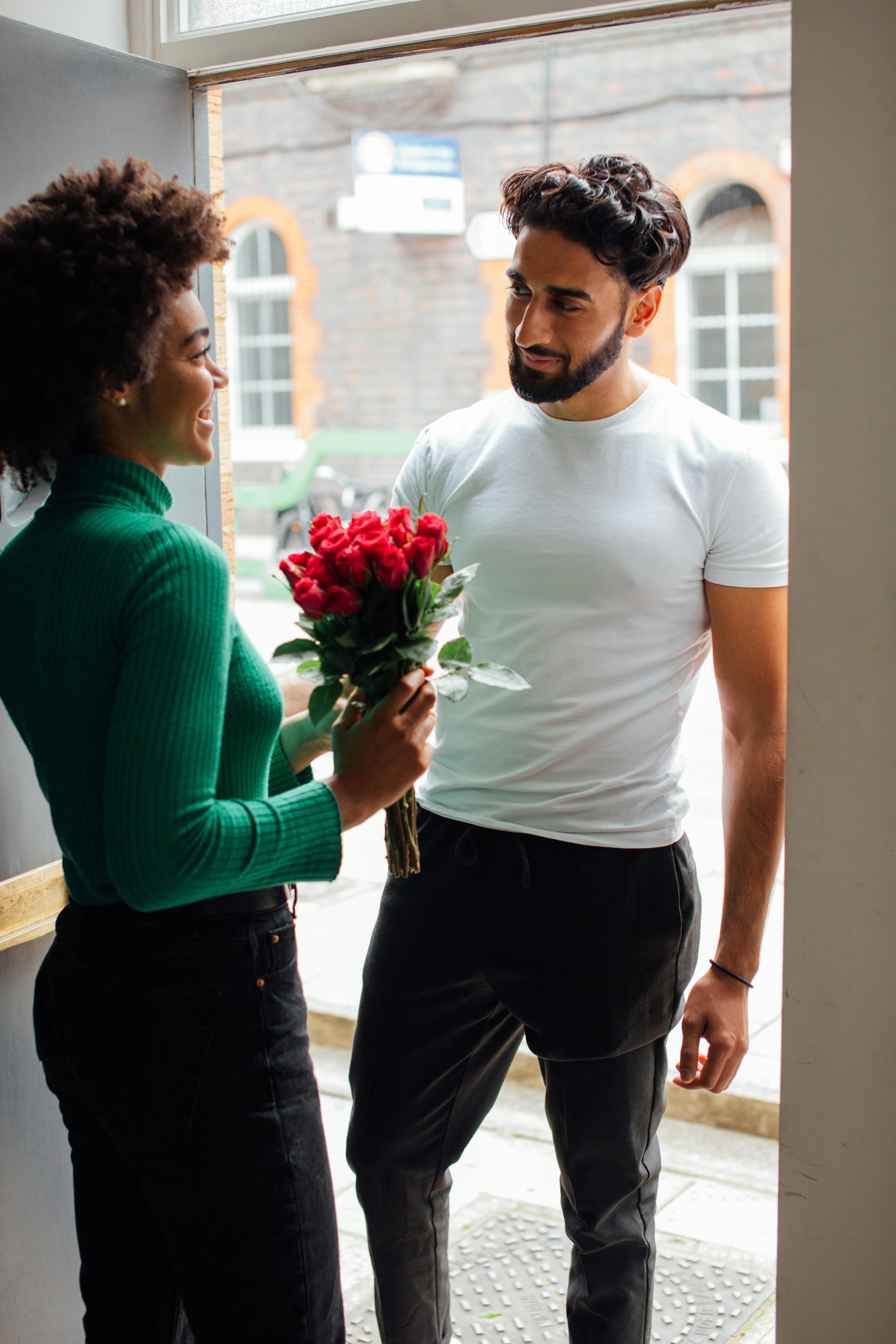 Couple sharing a romantic moment indoors, exchanging a bouquet of red roses.
