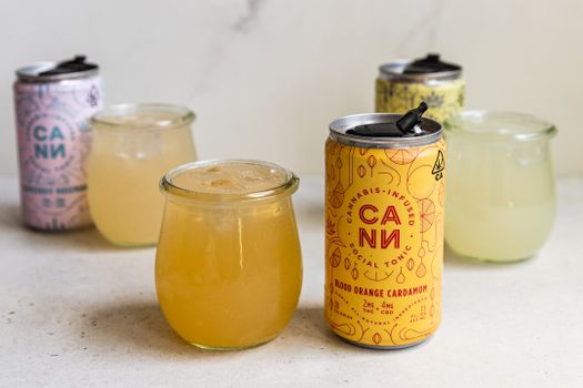 Vibrant display of cannabis-infused drinks in cans and glasses, featuring Blood Orange Cardamom flavor.