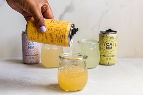 Person Holding Yellow Labeled Can with Liquid