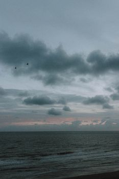 海面宁静，浪涛低缓，远处是阴云密布下的红色落日