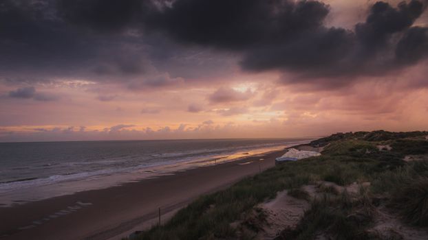 Breathtaking view of sea with foamy waves and sandy coast under colorful cloudy sky in evening