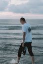 黄昏时分，一位无名赤脚游客在多云的天空下漫步，背影映在波纹起伏的海面上