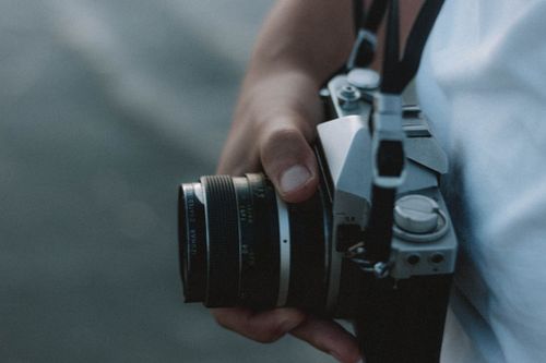 Free From above side view of crop unrecognizable person with aged photo camera on blurred background Stock Photo