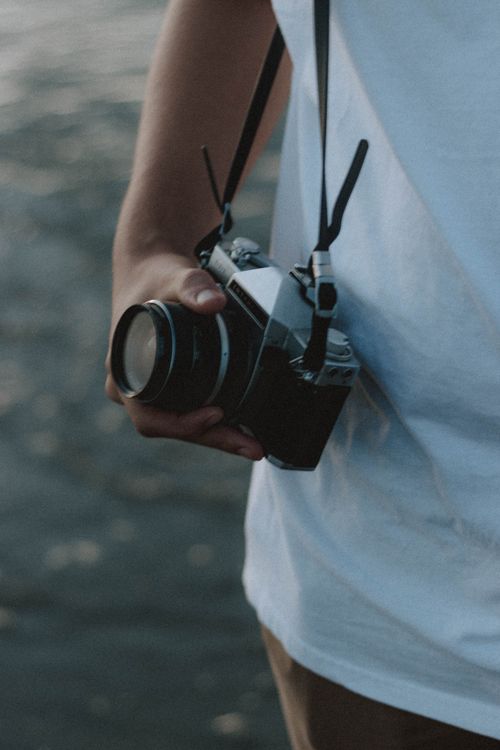 Free From above of crop unrecognizable traveler with retro photo camera near rippled sea in daylight Stock Photo