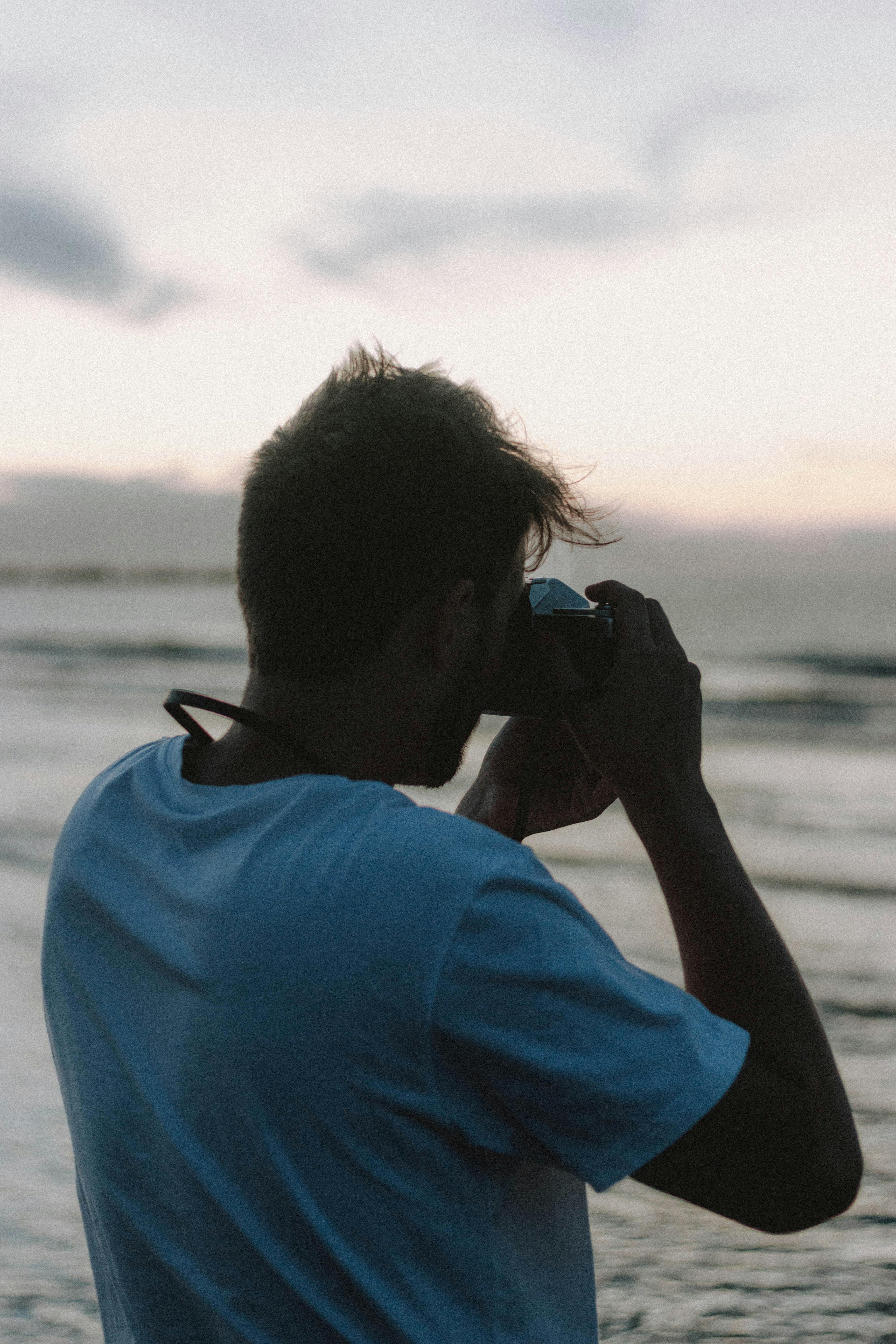 anonymous man taking photo of sea in evening time