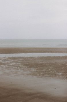 Empty coast of sandy beach during low tide in overcast weather against cloudless sky