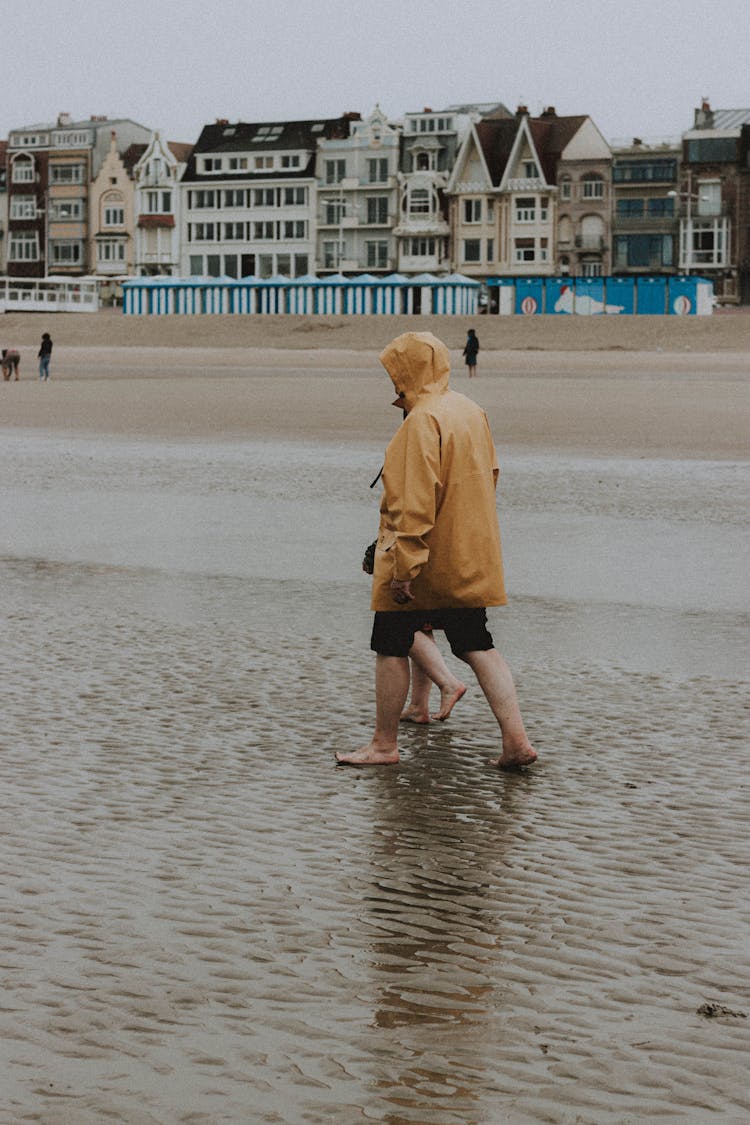 Barefoot Couple In Raincoats Walking On Beach