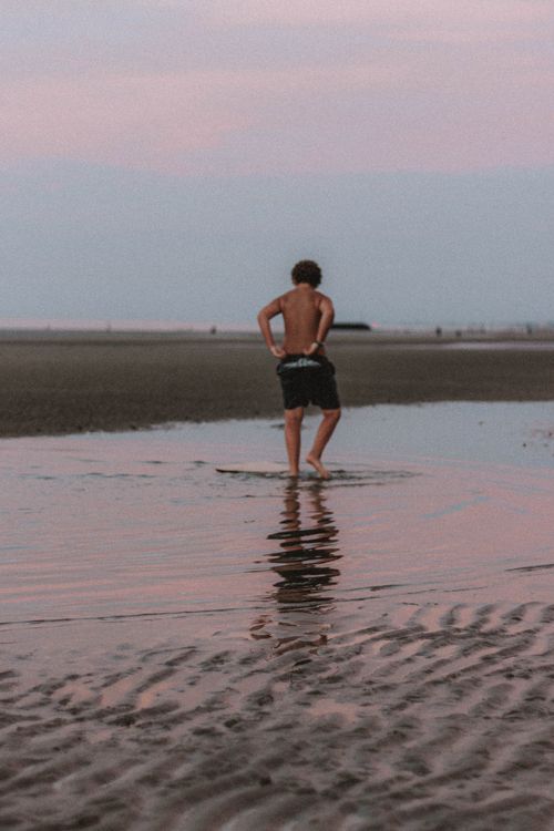 Free Back view of unrecognizable barefoot male in shorts strolling along sandy beach against sunset sky in evening time in summer Stock Photo