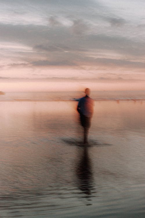 Silhouette of unrecognizable male standing in rippling sea against pink sky in sundown time in tropical country in summer evening