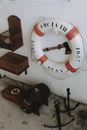 From above of hatchet in middle of lifebuoy with red inserts on white wall near wooden shelves and small anchors