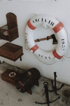 From above of hatchet in middle of lifebuoy with red inserts on white wall near wooden shelves and small anchors