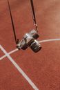 Old fashioned photo camera hanging on black strap against red ground with marking on stadium in daylight in summer day