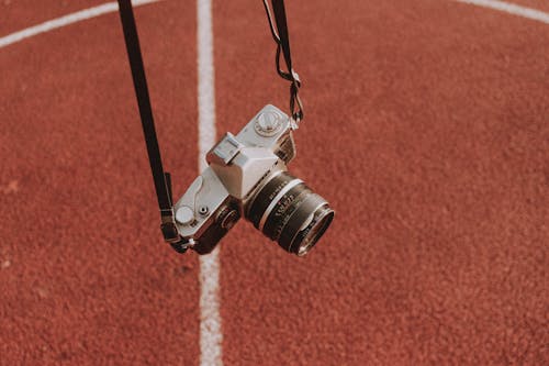 Aged photo camera fixed on thin leather belts above textured sports ground in daylight