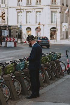 A businessman in a suit rents a bike from a city stand during a sunny day.
