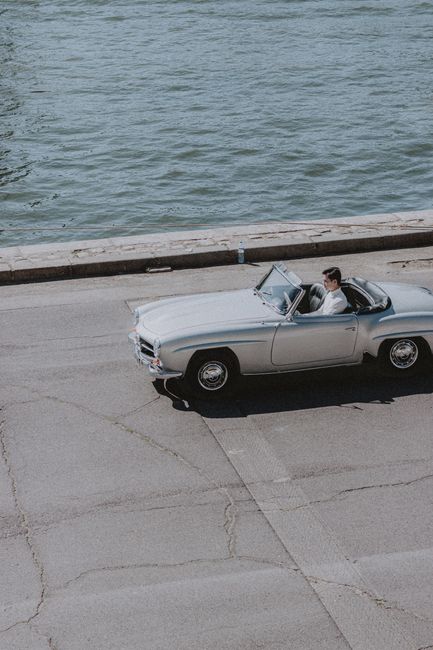 Young male riding vintage cabriolet on concrete berth near river on clear sunny afternoon