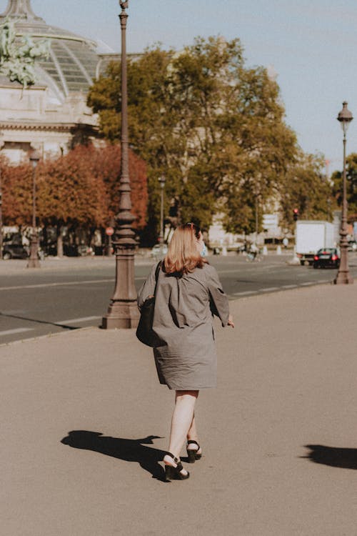 Back view of female in formal summer dress crossing pavement with vintage lampposts