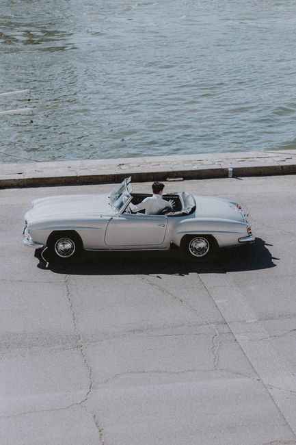 Young male on vintage light automobile with open top moving on sunny pier near water