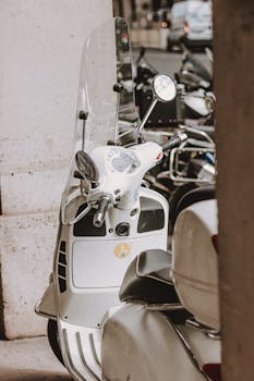 A retro white scooter with a windshield parked in a city street, offering a nostalgic urban vibe.