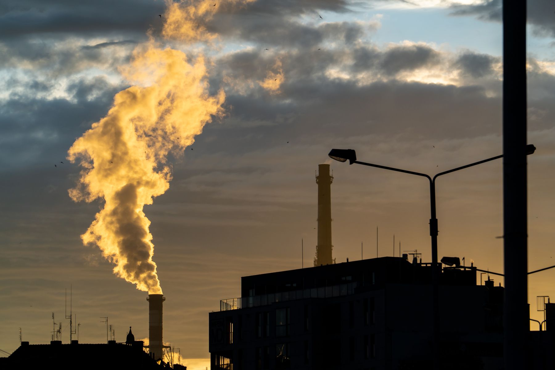Plant chimney and rooftops silhouetted against a golden dusk sky, photo by Piotr Twardowski on Pexels