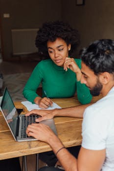 A collaborative work session between two adults using a laptop indoors.