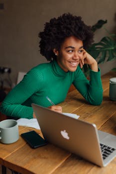 African American woman with afro hair smiling while working on a laptop indoors.