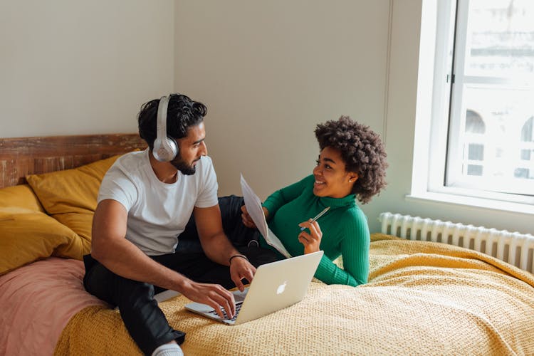 A Couple Having Conversation While Working On The Bed Together