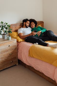 A couple lies together on a comfortable bed in a bright, cozy bedroom setting.