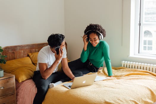 Young couple collaborating on bed with laptop and phones indoors.