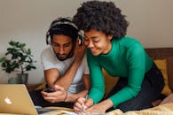 一对夫妇面带微笑，在家用笔记本电脑和耳机工作