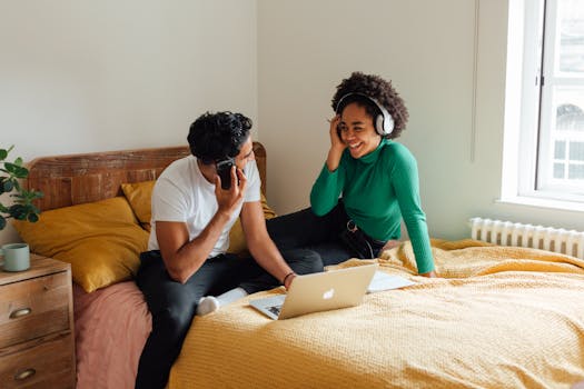 Happy couple with headphones and laptop relaxing in a cozy bedroom setting.