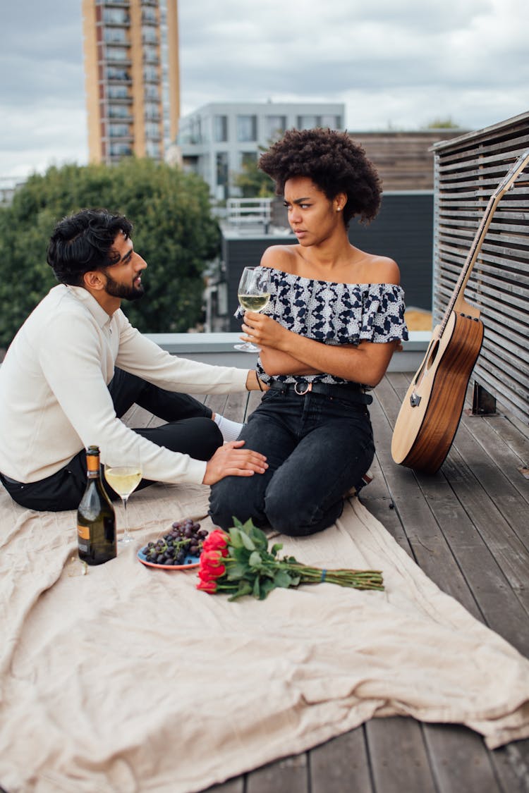 Man And Woman Sitting On Wooden Rooftop With Picnic Blanket