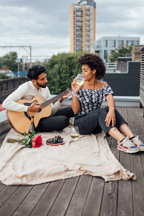 Uomo E Donna Che Si Siede Sulla Panchina Mentre Si Suona La Chitarra Acustica