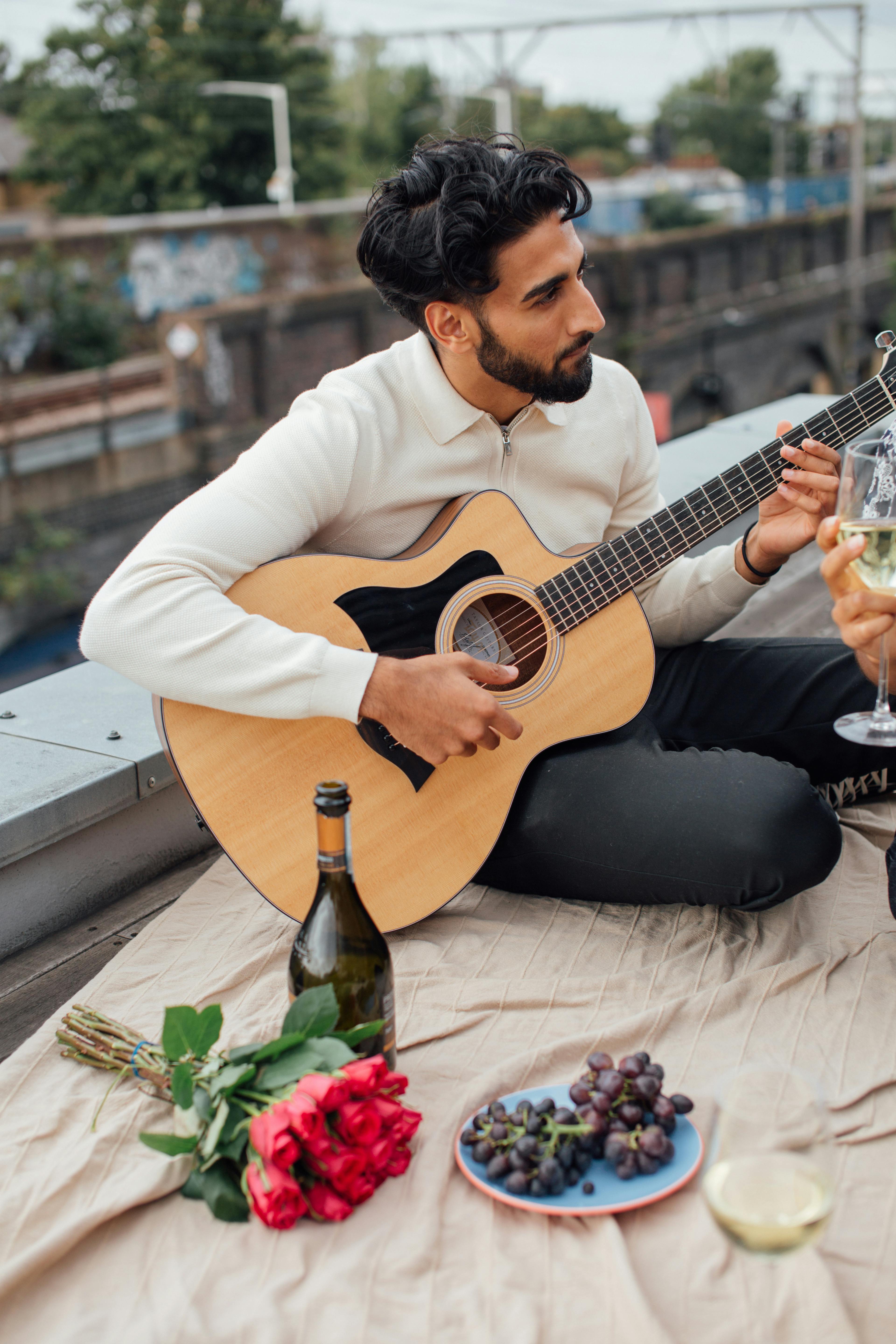Man playing acoustic guitar on a rooftop with wine and roses. Ideal for lifestyle and leisure themes.