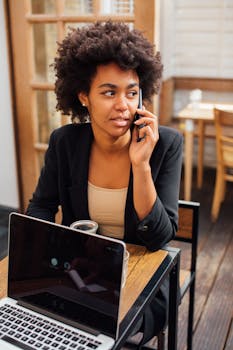 Businesswoman talking on phone while working on a laptop in a café.