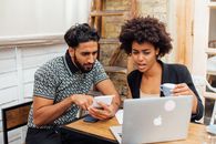 Man and Woman Sitting at Table Using Macbook