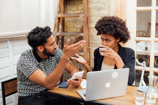 Two colleagues having a discussion while working on a laptop in an office space.