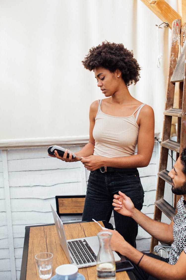 Man Sitting At The Desk With A Laptop And Woman Holding A Payment Terminal 