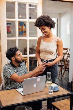 A man and woman smiling during a transaction using a pay terminal in a cozy cafe.
