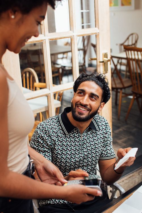 Free Man smiles while making a contactless payment in a cozy cafe setting. Stock Photo