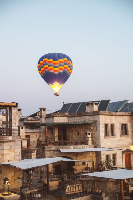 Scenic view of a colorful hot air balloon flying over Cappadocia's stone buildings at sunrise.