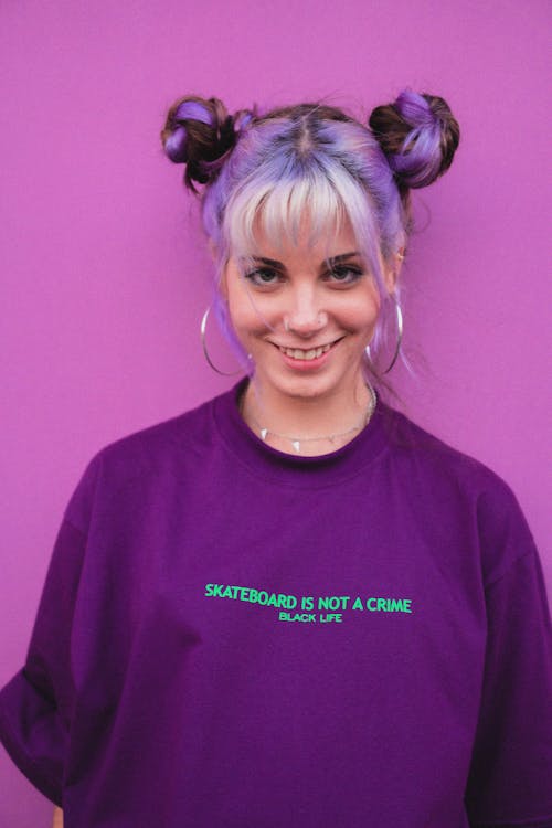 Young happy extraordinary female with dyed hairstyle and earrings looking at camera on purple background