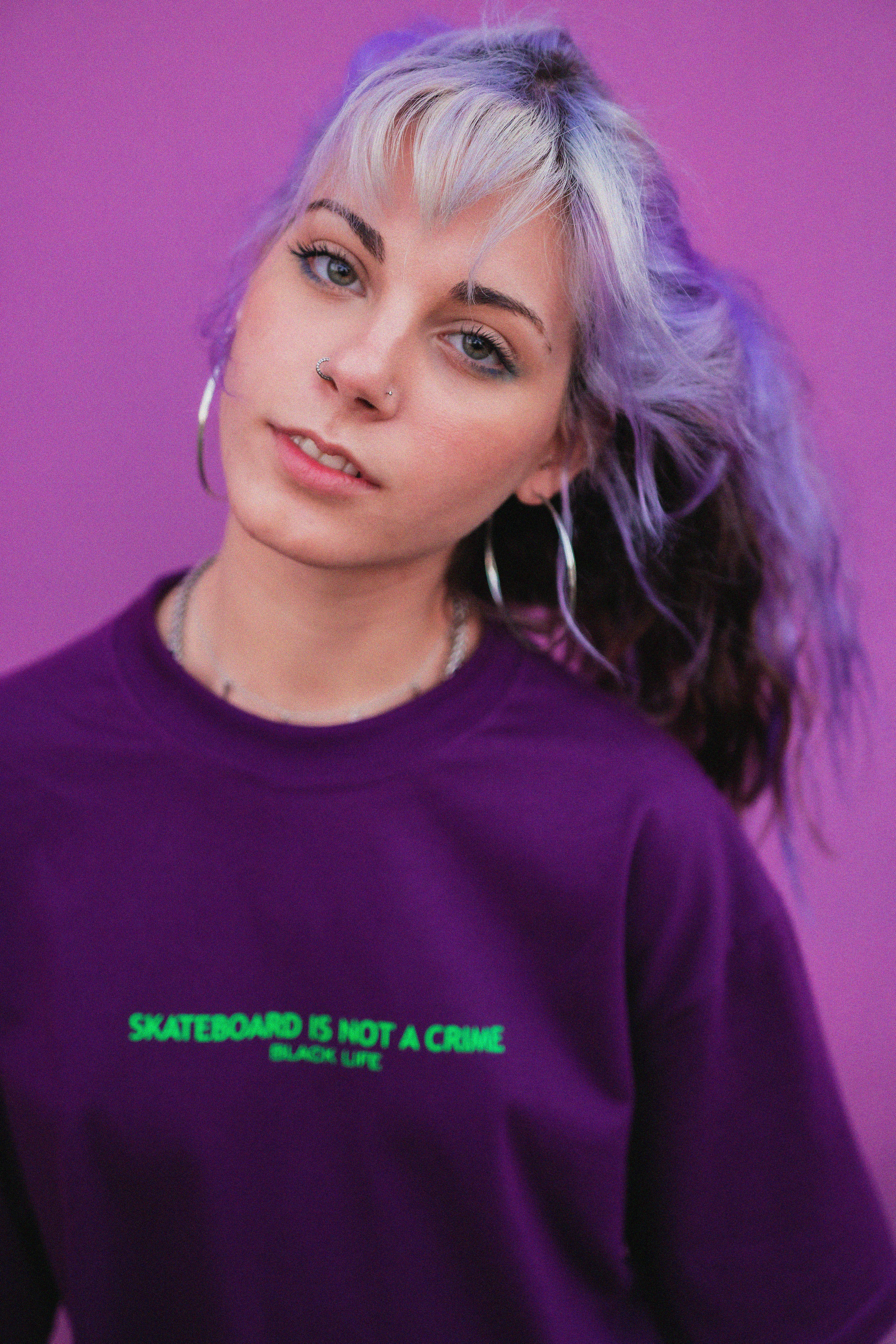Positive young female with ash blond hair in trendy hoodie posing and looking at camera on purple background
