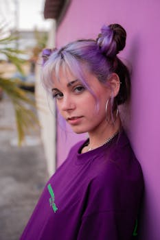 一位迷人的非正式女性，染着头发，倚靠在花园里被弄脏的紫色背景墙上，看着照相机